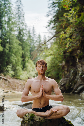 White man wearing swimming trunks meditating while resting by river