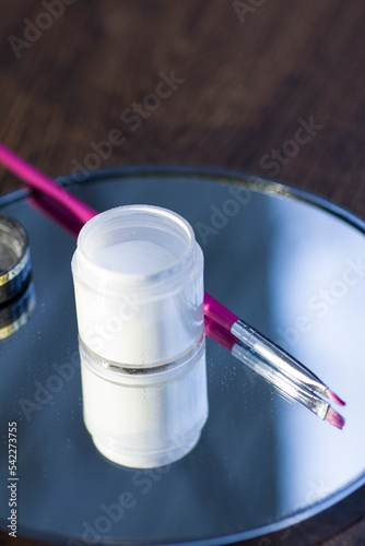 White acrylic powder to strengthen the nail plate and a brush in the reflection of the mirror