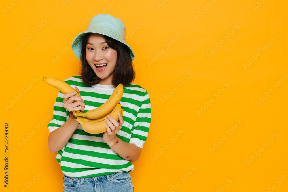 Asian young woman wearing panama smiling while holding bananas Asian young woman wearing panama smiling while holding bananas