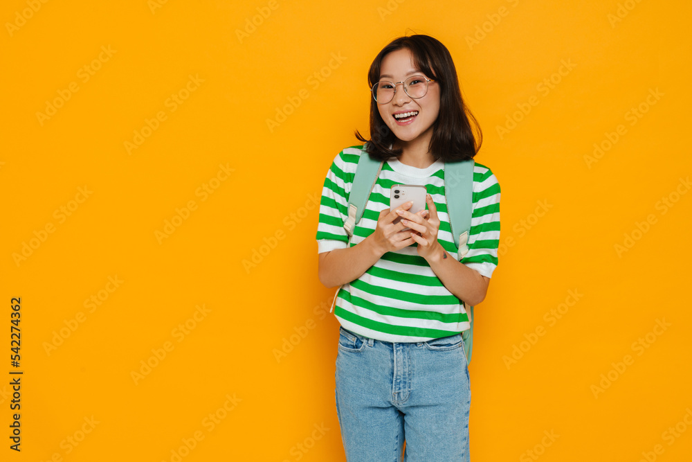 Asian pleased female student smiling while using mobile phone Asian pleased female student smiling while using mobile phone