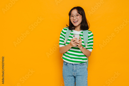 Asian pleased female student smiling while using mobile phone