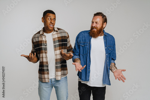 Two multinational displeased men gesturing while looking at each other isolated