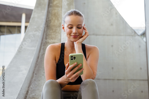 Young beautiful smiling sporty woman holding and using her phone