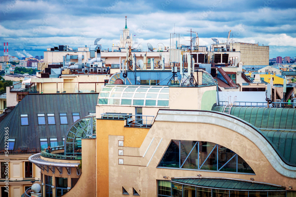 Obraz premium Roofs of houses of a large metropolis with pipes and TV antennas against a blue sky with clouds.