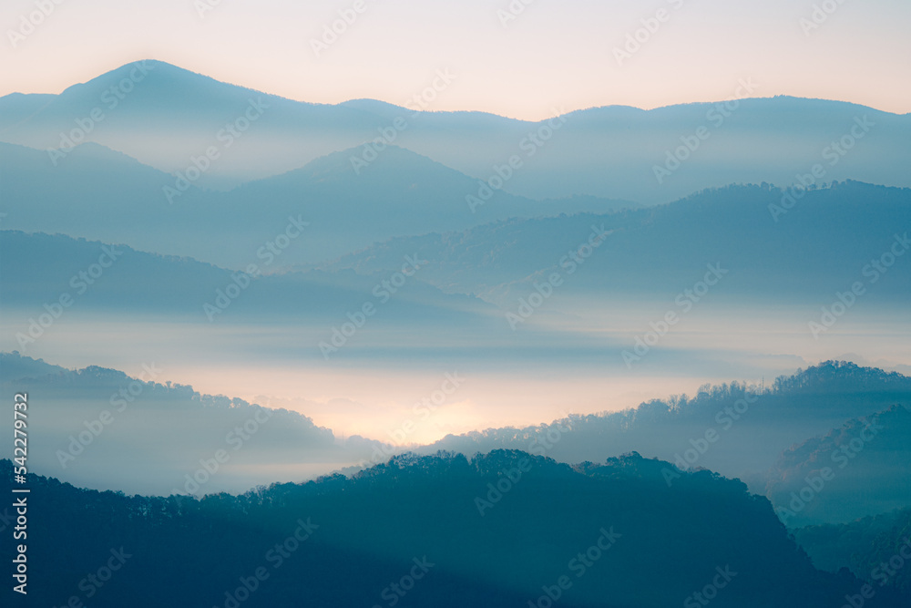 A blue and orange glowing view of layers of mountains in the Smoky Mountains in North Carolina. There is a lot of haze and fog in the mountain valleys. 