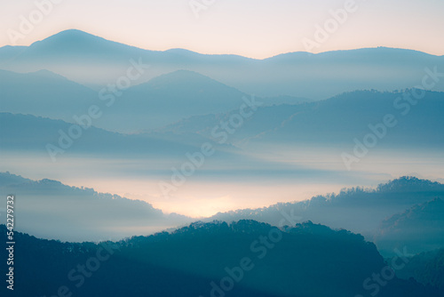 A blue and orange glowing view of layers of mountains in the Smoky Mountains in North Carolina. There is a lot of haze and fog in the mountain valleys. 