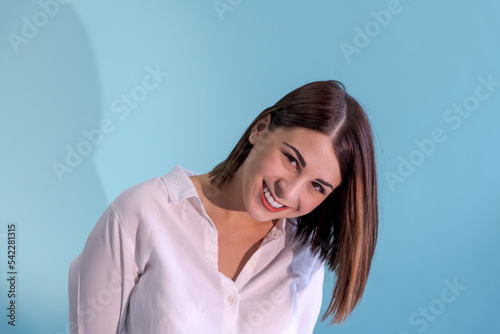Close-up portrait of beautiful smiling caucasian woman with brown hair wearing white shirt. Blue background. Selective focus. People theme.