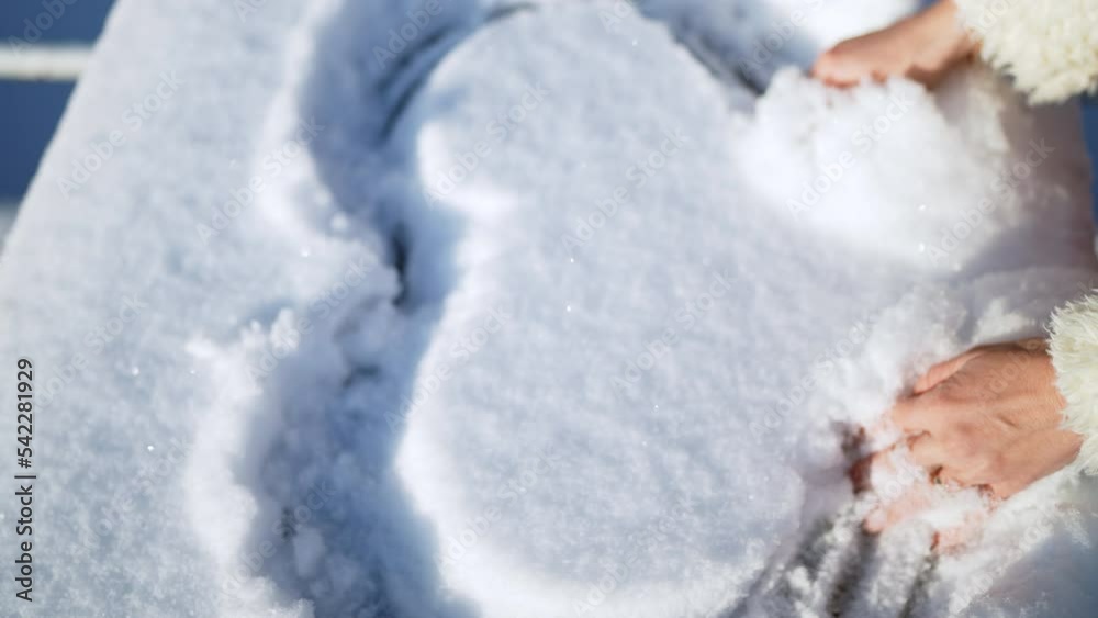 female hands draw a heart on the snow on a cold winter sunny morning close-up female hands draw a heart on the snow on a cold winter sunny morning close-up