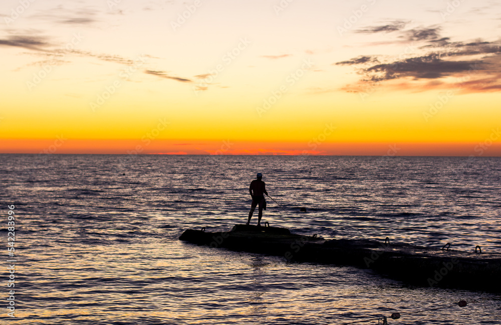  silhouette of  man on  pier by  sea against  sunset.  male fisherman holds  fishing rod,  beautiful seascape.  lonely man.