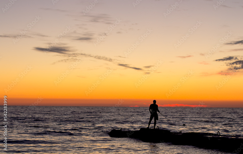  silhouette of  man on  pier by  sea against  sunset.  male fisherman holds  fishing rod,  beautiful seascape.  lonely man.