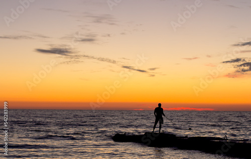  silhouette of man on pier by sea against sunset. male fisherman holds fishing rod, beautiful seascape. lonely man.