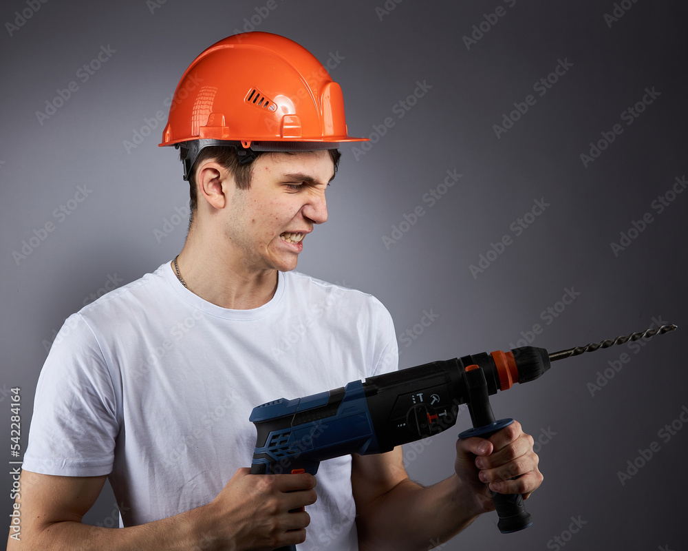 a young construction worker in a hard hat and a white T-shirt with a puncher in his hand. a young construction worker in a hard hat and a white T-shirt with a puncher in his hand.