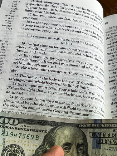 The Holy Bible in English with a tab from the $ 100 banknote showing a passage from the Gospel according to St. Matthew 6:24 photo