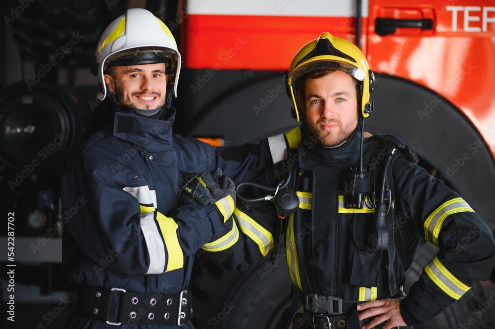 Two firefighters in protective clothing in helmets with fire engine, friendly handshake