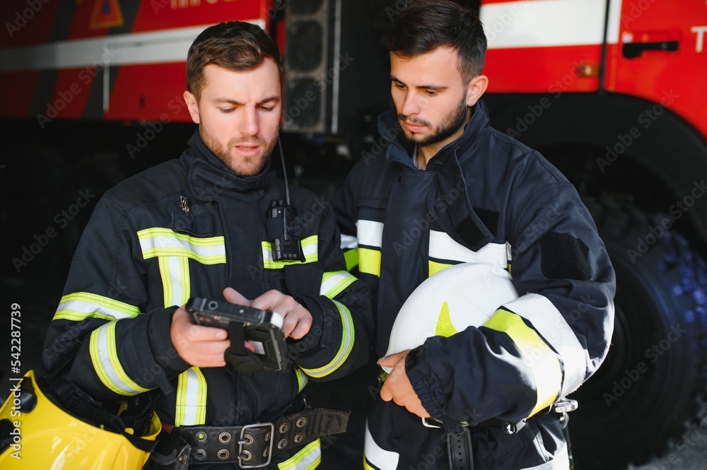 Portrait of two firefighters in fire fighting operation, fireman in protective clothing and helmet using tablet computer in action fighting Portrait of two firefighters in fire fighting operation, fireman in protective clothing and helmet using tablet computer in action fighting