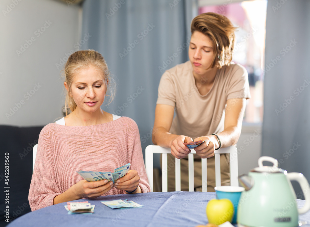 Fototapeta premium Portrait of woman giving money to son, chatting at table indoors