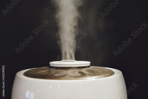 A working white humidifier on a black background, water vapor close-up