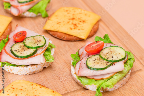 Light Breakfast. Quick and Healthy Sandwiches. Rice Cakes with Ham, Tomato, Fresh Cucumber, Green Salad and Cheese on Wooden Cutting Board. Beige Background