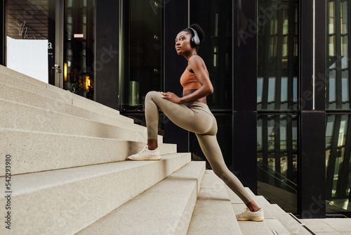 Young beautiful calm african woman in headphones stretching her legs