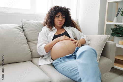 Pregnant woman smile and happiness sits on the couch freedom and strokes her belly feels kicks with the baby in the last month of pregnancy, mother's day lifestyle