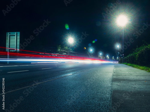 Night city scene with road and car light trail. Dark night sky. Town traffic. Moody blue color tone.