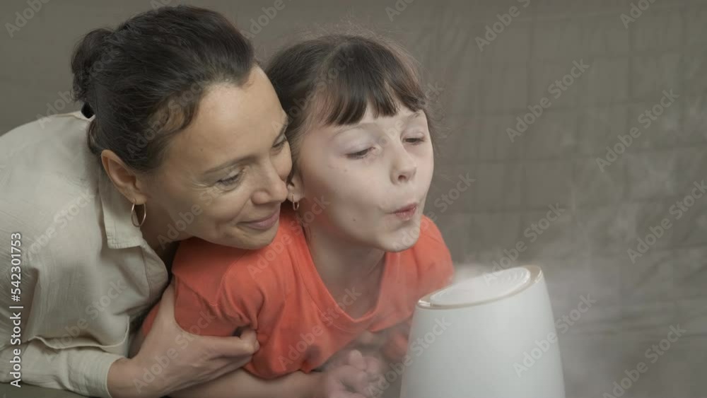 Prevention of infections with humidifier. A child with her mother blow at steam from the air purifier in the modern room. Prevention of infections with humidifier. A child with her mother blow at steam from the air purifier in the modern room.