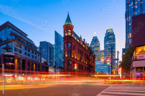 Obraz na płótnie Canada, Toronto. The famous Gooderham building and the skyscrapers in the background. View of the city in the evening. Blurring traffic lights. Modern and ancient architecture. Night city. w salonie