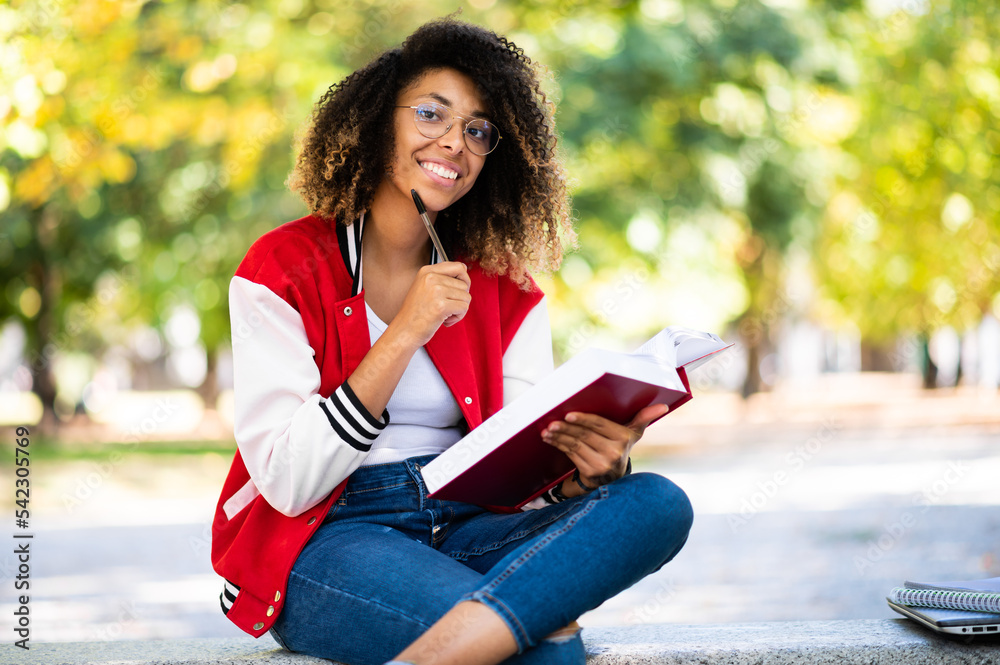 Beautiful african female college student reading a book on a bench in a park Beautiful african female college student reading a book on a bench in a park