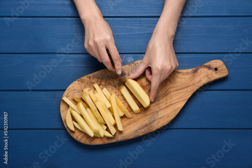 Woman cutting potato at blue wooden table, top view. Cooking delicious French fries