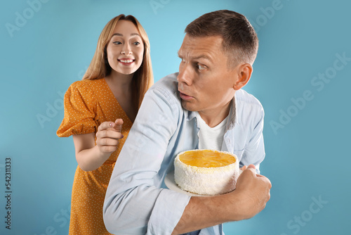 Photos Greedy man hiding tasty cake from woman on turquoise background