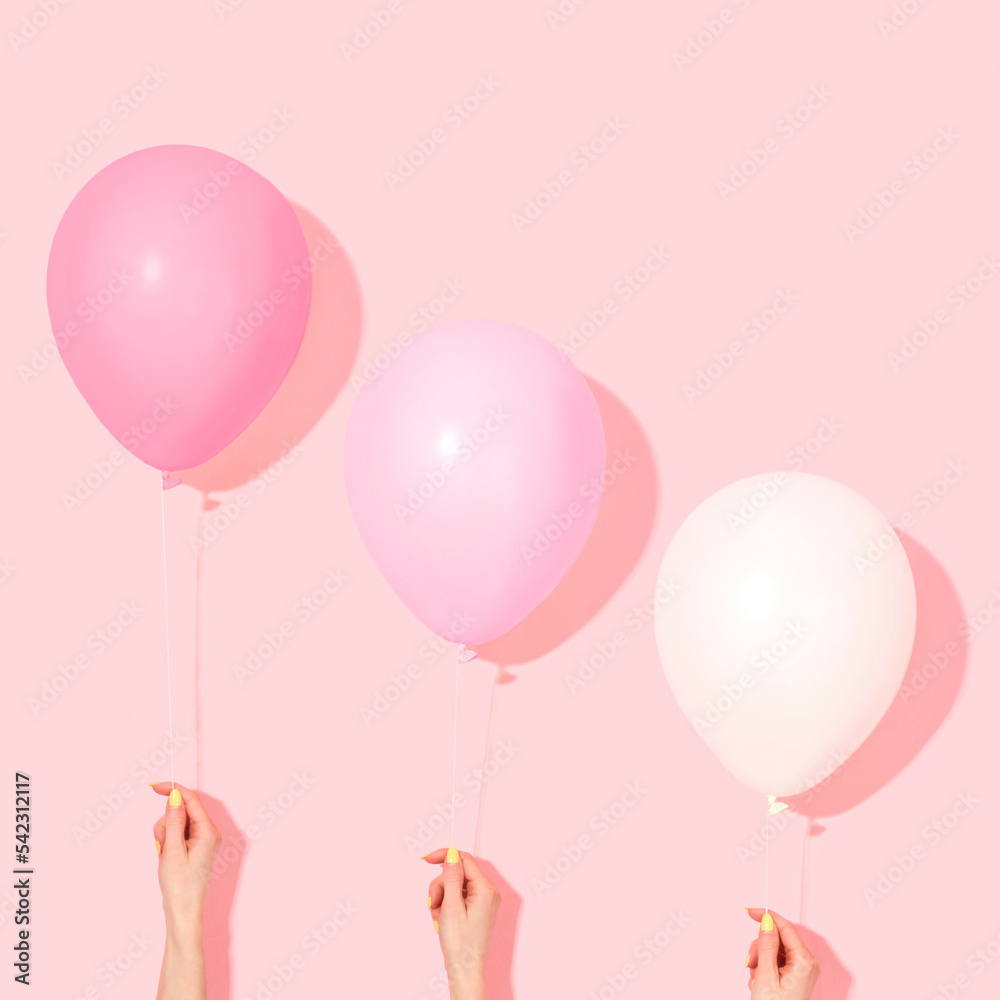 Pastel pink and white balloons with female hands. Minimal style pink color balloons floating out from the floor on pink background. Surreal modern still life