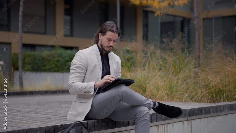 Employee man drinking coffee and working tablet computer at the street. Confident executive chatting with partner on his digital device. Corporate lifestyle concept Employee man drinking coffee and working tablet computer at the street. Confident executive chatting with partner on his digital device. Corporate lifestyle concept