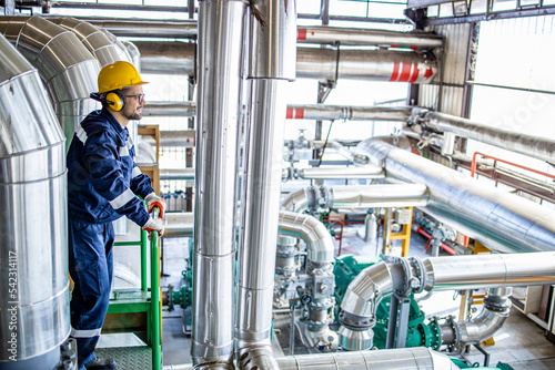 Foto Refinery worker standing on metal bridge platform and controlling energy production inside heating plant