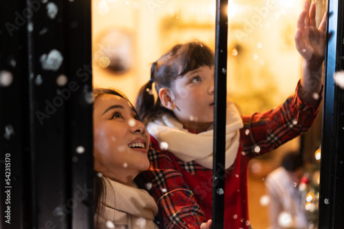 Adorable child looking at the window and first snow flakes with mother.