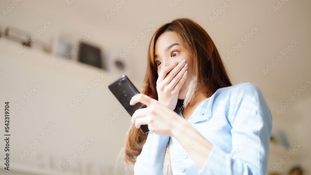 Funny euphoric young asian woman celebrating winning or getting ecommerce shopping offer on mobile smartphone. Excited happy girl winner looking smart phone celebrating success Funny euphoric young asian woman celebrating winning or getting ecommerce shopping offer on mobile smartphone. Excited happy girl winner looking smart phone celebrating success