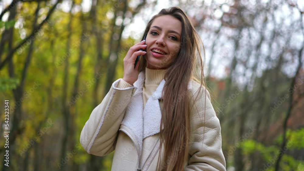Positive attractive brunette speaking on the phone smiling outdoors. Lady touches her hair looking into camera and holding her phone at the ear. Positive attractive brunette speaking on the phone smiling outdoors. Lady touches her hair looking into camera and holding her phone at the ear.