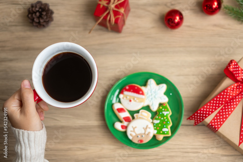 Merry Christmas with woman hand holding coffee cup and homemade cookie on table. Xmas eve, party, holiday and happy New Year concept