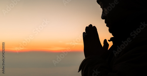 Concept Christian person worship or pray to God. Christian man silhouette with love, faith, devotion to God with sunrise sky background.Male worship God for peace, victory, success with hope. religion