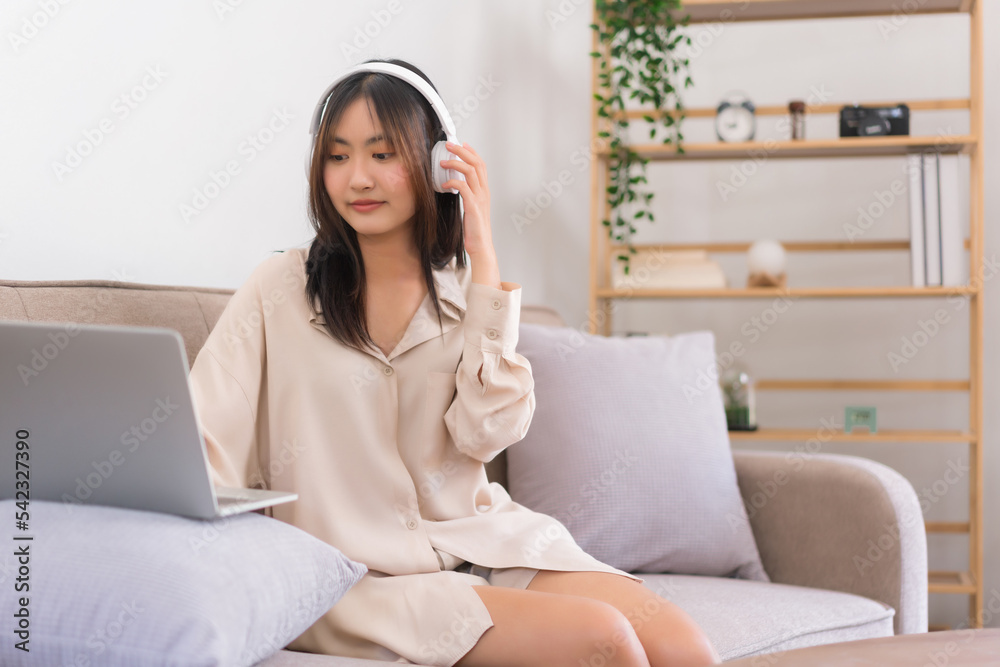 Concept of activity in living room, Asian woman is listening music and chat with friend on laptop Concept of activity in living room, Asian woman is listening music and chat with friend on laptop