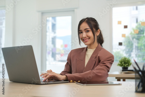 Beautiful businesswoman sitting front of laptop computer and smiling to camera.