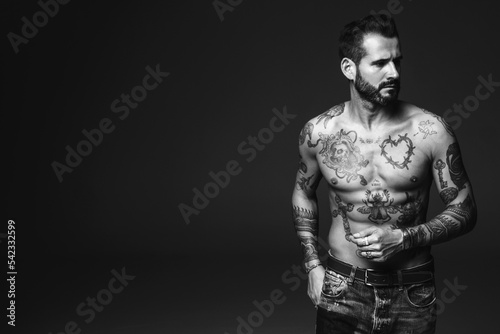Portrait of handsome confident stylish hipster lambersexual model. Sexy modern man. Naked torso with tattoos.Fashion male posing in studio on dark background © halayalex