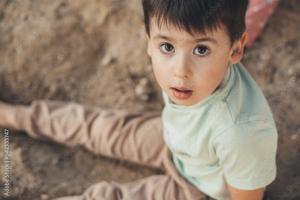 Portrait of a boy sitting in the sand looking into the camera. People lifestyle concept. Happiness concept. Family lifestyle concept. Family activity concept Portrait of a boy sitting in the sand looking into the camera. People lifestyle concept. Happiness concept. Family lifestyle concept. Family activity concept