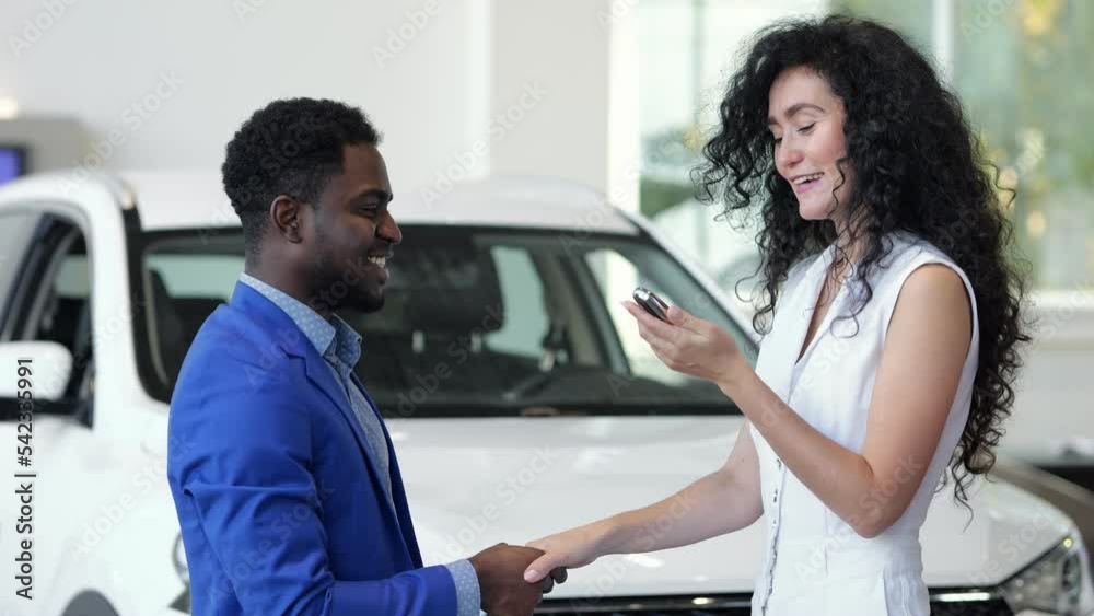 African American salesman gives key to bought car to happy and excited female customer in automobile salon. Woman satisfied with new purchase African American salesman gives key to bought car to happy and excited female customer in automobile salon. Woman satisfied with new purchase