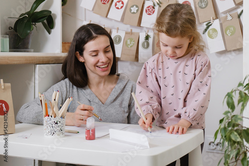 toddler child writing Christmas letter and doing advent calendar tasks in kids room. Festive activities for kids at home. Happy dreaming girl creating art craft
