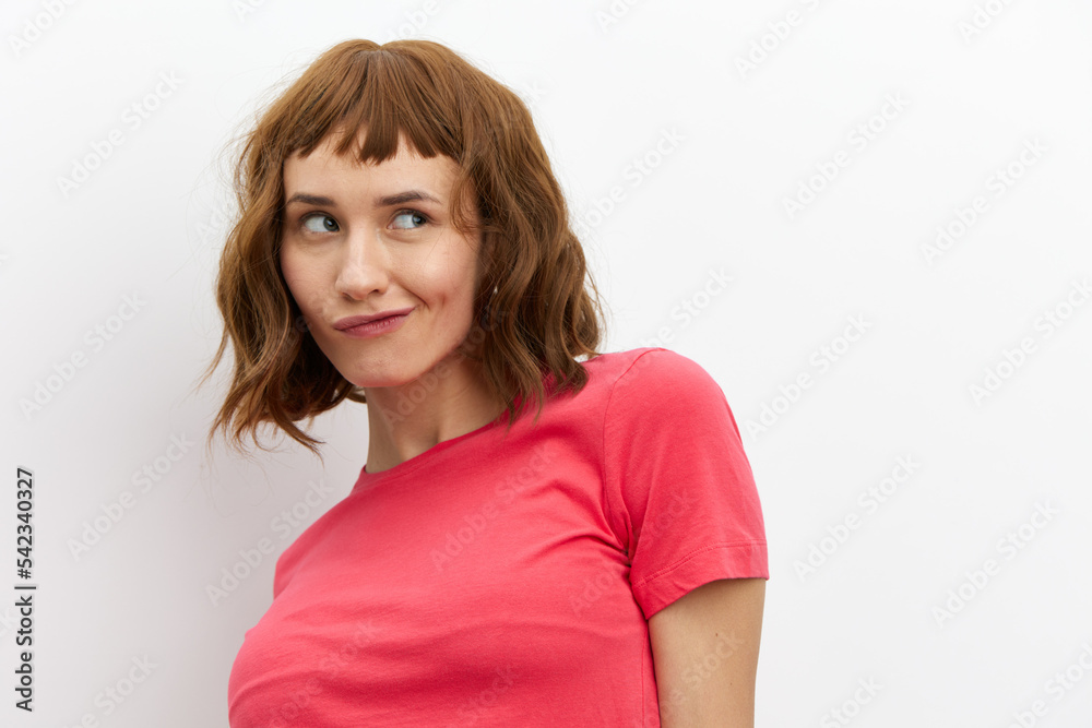 Obraz premium a funny, mischievous woman in a red T-shirt stands on a white background playfully looking away