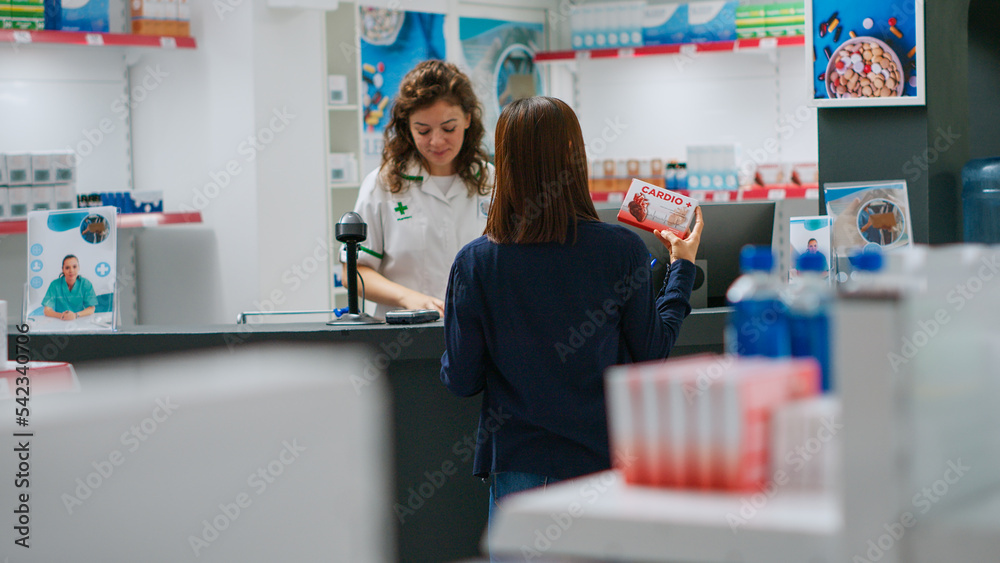 Asian woman reading cardiology pills leaflet to buy medicaments in pharmacy shop, looking at vitamins box and supplements. Client checking pharmaceutics products in drugstore. Handheld shot.