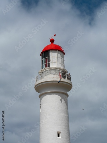 White lighthouse with red roof by the coast, vertical