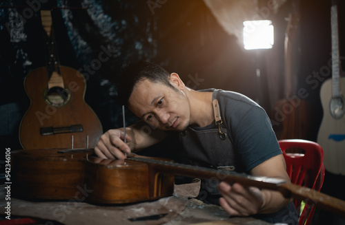Guitar makers asian man making acoustic guitars in laboratory. Asian guitar maker builds high quality guitars for musicians handmade guitar shop. Working fine woodusic, tradition, ancient crafts.