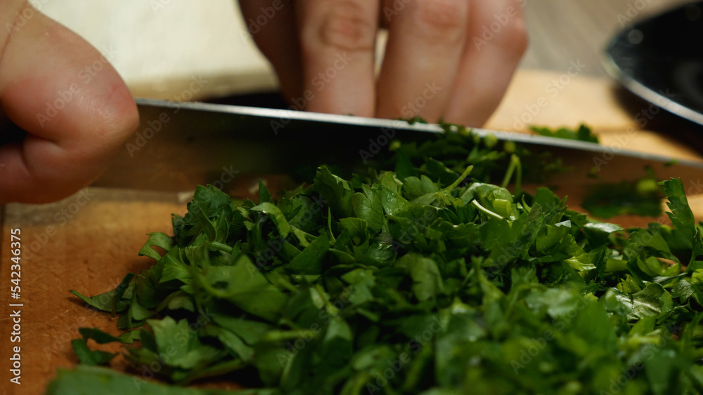 Close-up of a cook slicing parsley with a knife on a cutting board. Side view. Delicious and healthy food. Close-up of a cook slicing parsley with a knife on a cutting board. Side view. Delicious and healthy food.