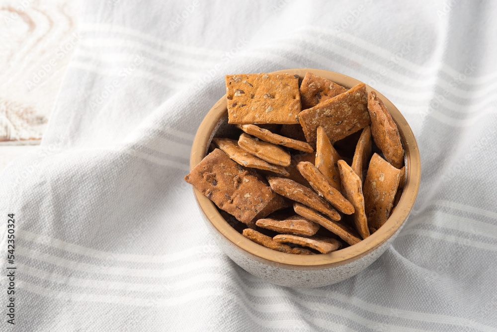 Bowl of dry crackers with tomato and basil on light wood background with napkin Bowl of dry crackers with tomato and basil on light wood background with napkin